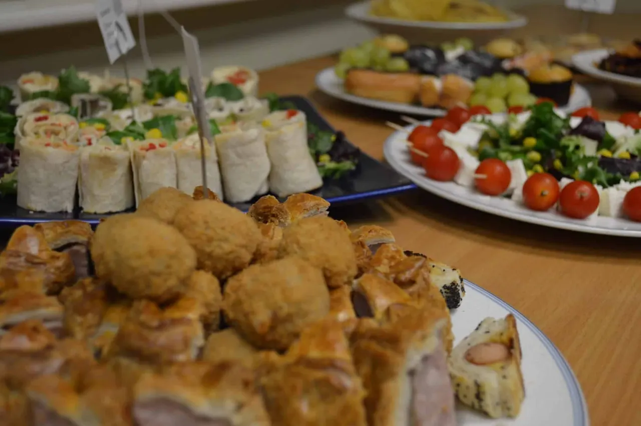 Buffet spread with fried meatballs in foreground, wraps, salads with tomatoes and olives, and other dishes on plates.