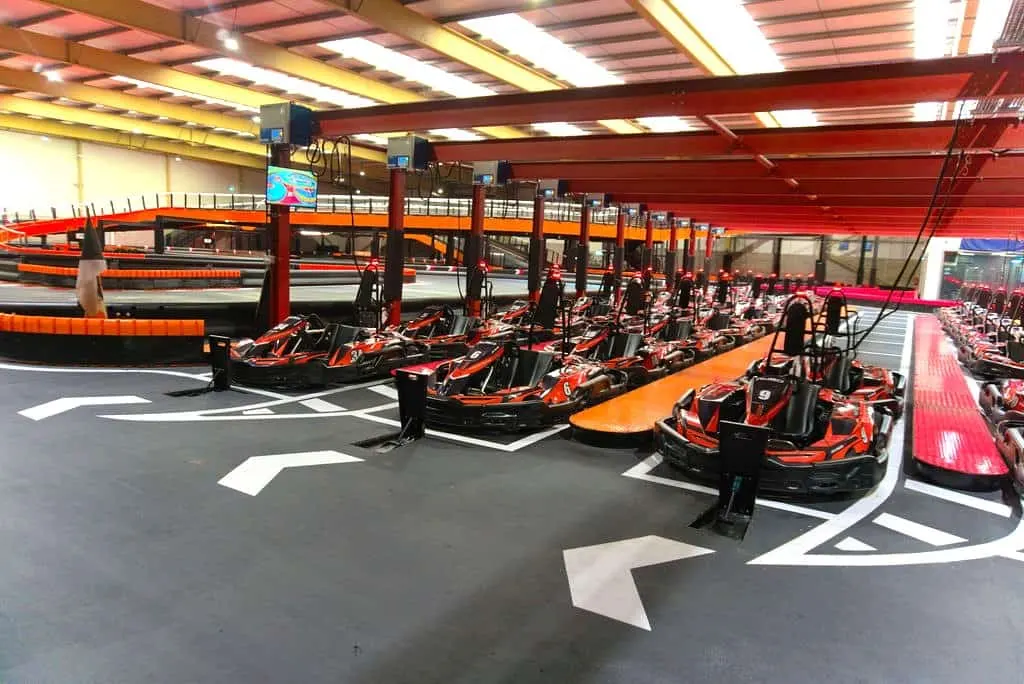Indoor go-kart racing facility with red and black karts lined up on a track marked with white directional arrows.