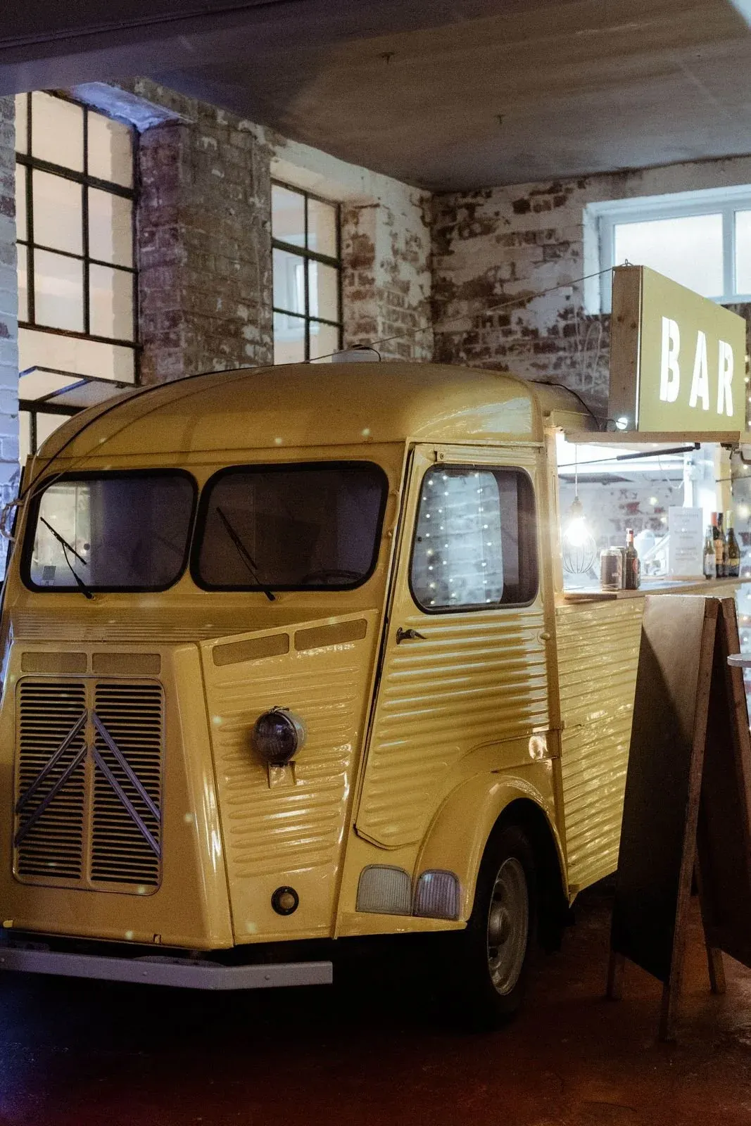 Vintage yellow food truck converted into a bar, displayed indoors against exposed brick walls.