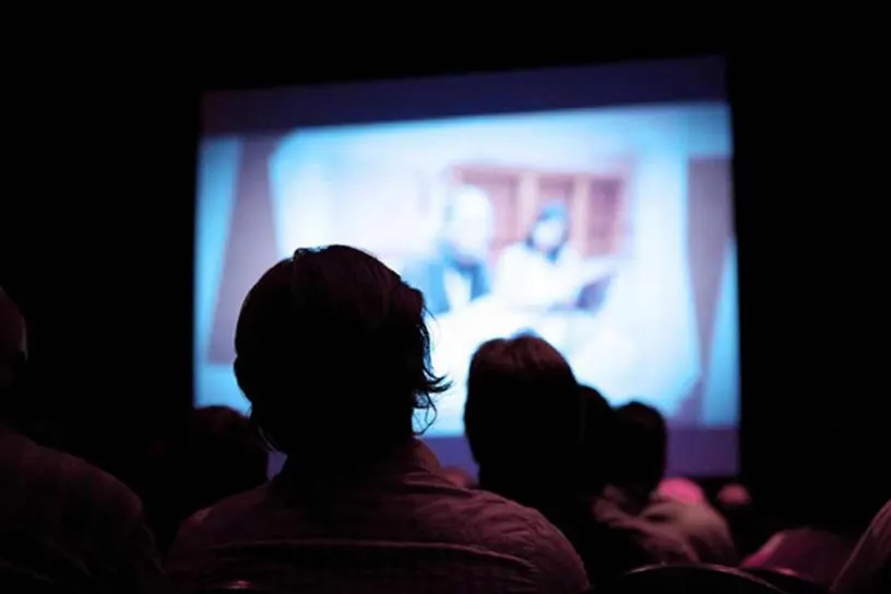 People sitting in a darkened cinema watching a film on a large screen.