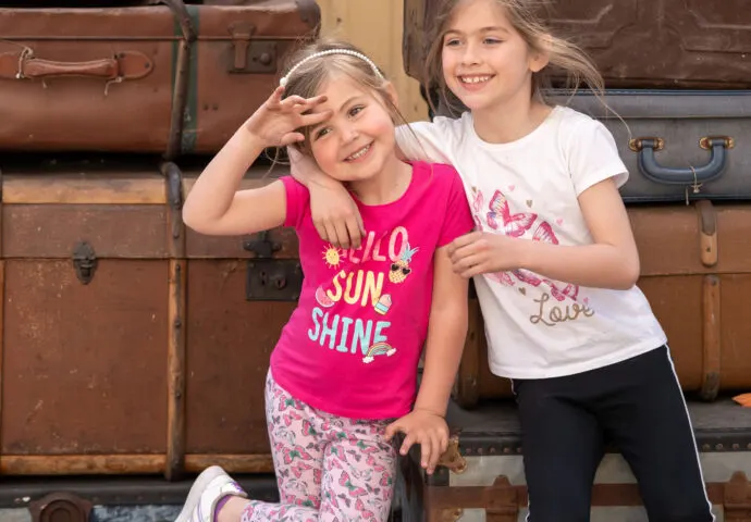 Two young girls posing together in front of stacked vintage suitcases at a heritage railway station.