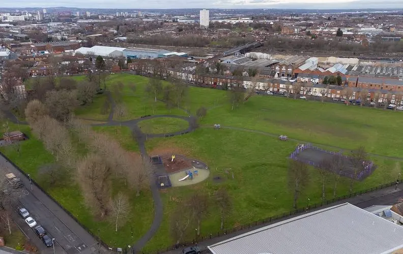 Aerial view of a public park with play equipment, winding paths, bare trees and surrounding residential streets.