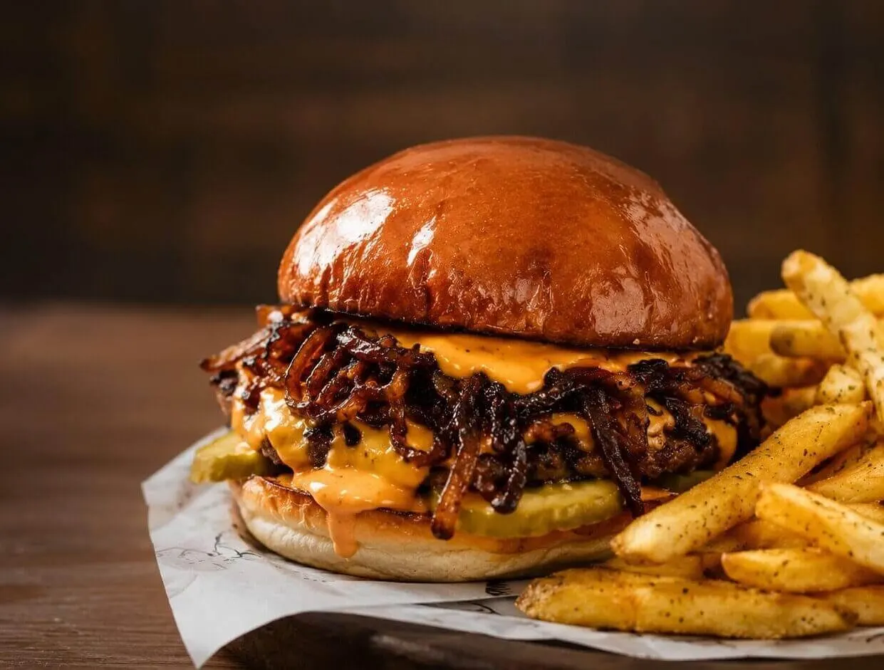 Burger topped with melted cheese and caramelised onions alongside chips, served on paper.