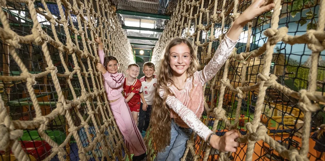 Four children navigating a rope obstacle course inside an indoor play structure.