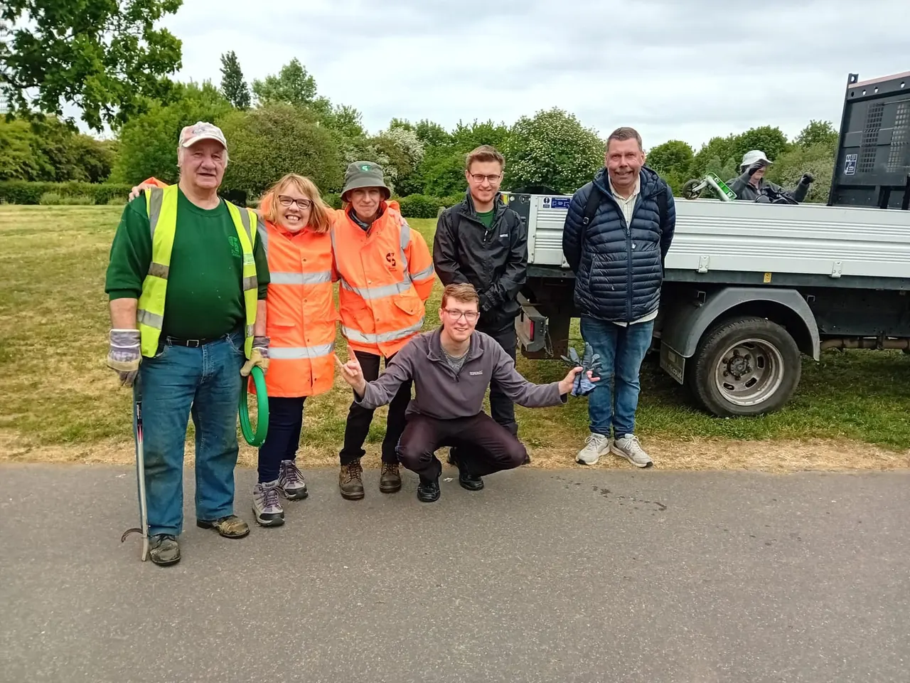 Group of volunteers and staff posing together outdoors at a park, with a utility truck and green spaces in the background.