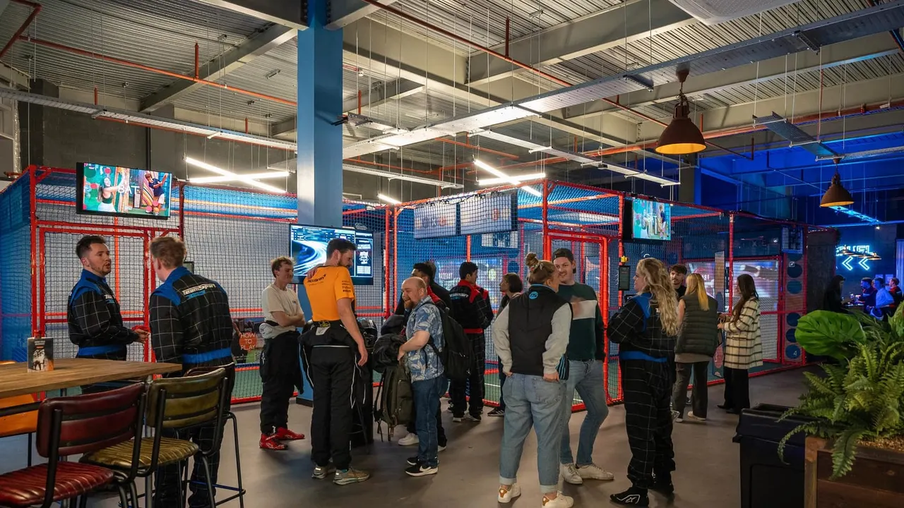 Group of visitors gathered inside an indoor cricket facility with red and blue netted bays.