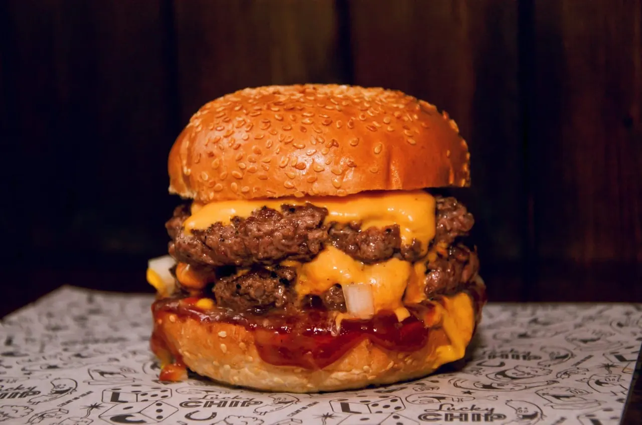 Double cheeseburger with two beef patties, melted cheese, and diced onions on a seeded bun.