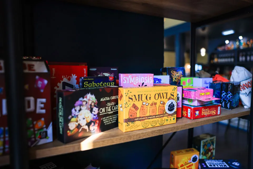 Board games and boxed games displayed on wooden shelving in a dimly lit games venue.