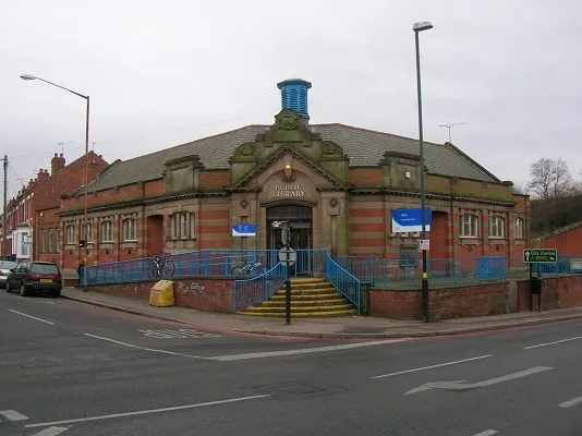 Historic red-brick library building with green roof and blue railings on a street corner.