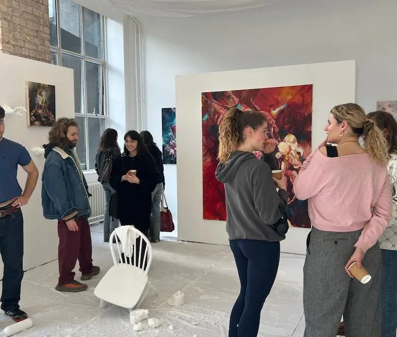 Visitors view contemporary artworks displayed on white walls in a bright gallery space with large windows.
