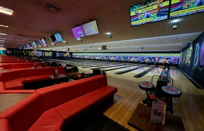 Interior of a ten-pin bowling alley with red seating, multiple lanes, and digital scoreboards overhead.