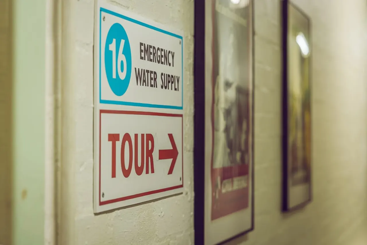 Directional signs mounted on an interior wall, one reading "Emergency Water Supply" with a number 16, and another reading "Tour 7" with an arrow.