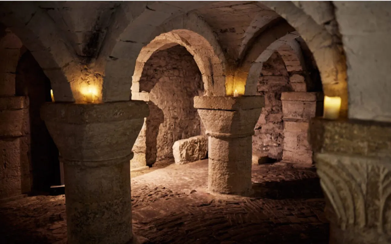 Underground stone archway with columns and warm lighting inside a historic castle prison.
