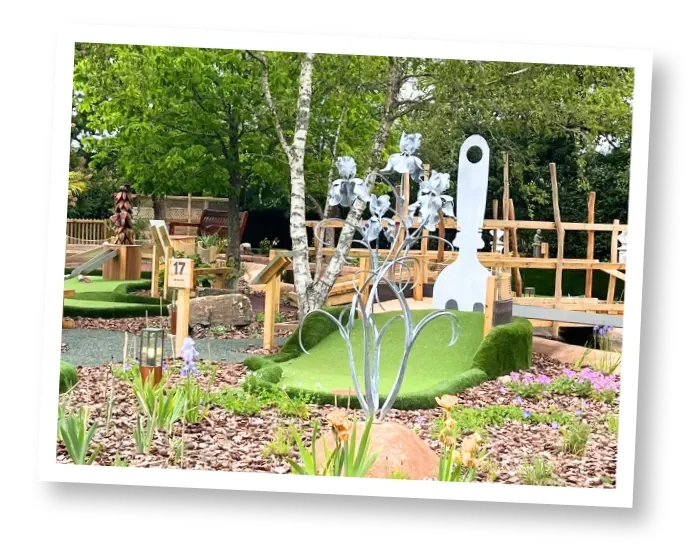 Outdoor adventure golf course with themed sculptural installations, wooden structures and landscaped garden areas.