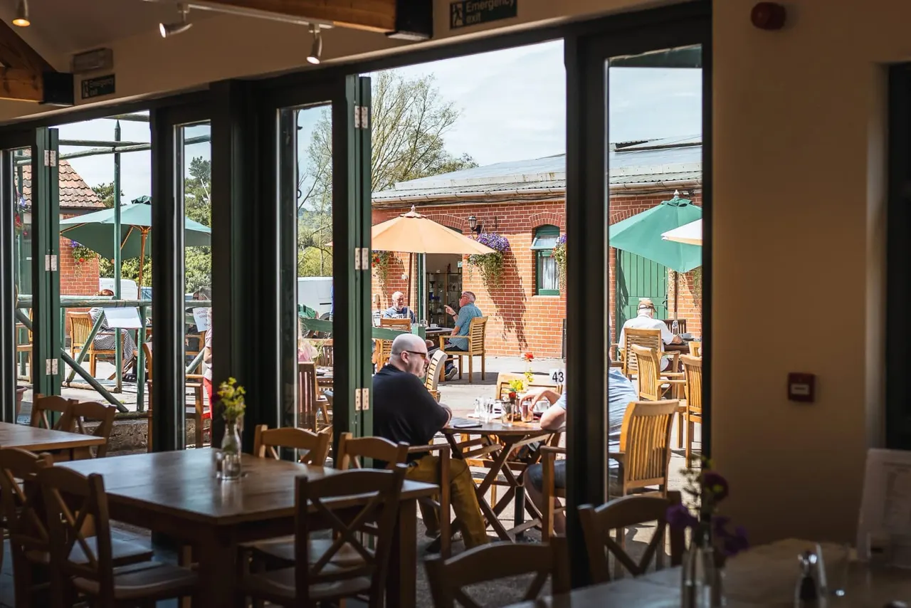 Interior dining room with glass doors opening onto a brick courtyard where diners sit at tables under parasols.