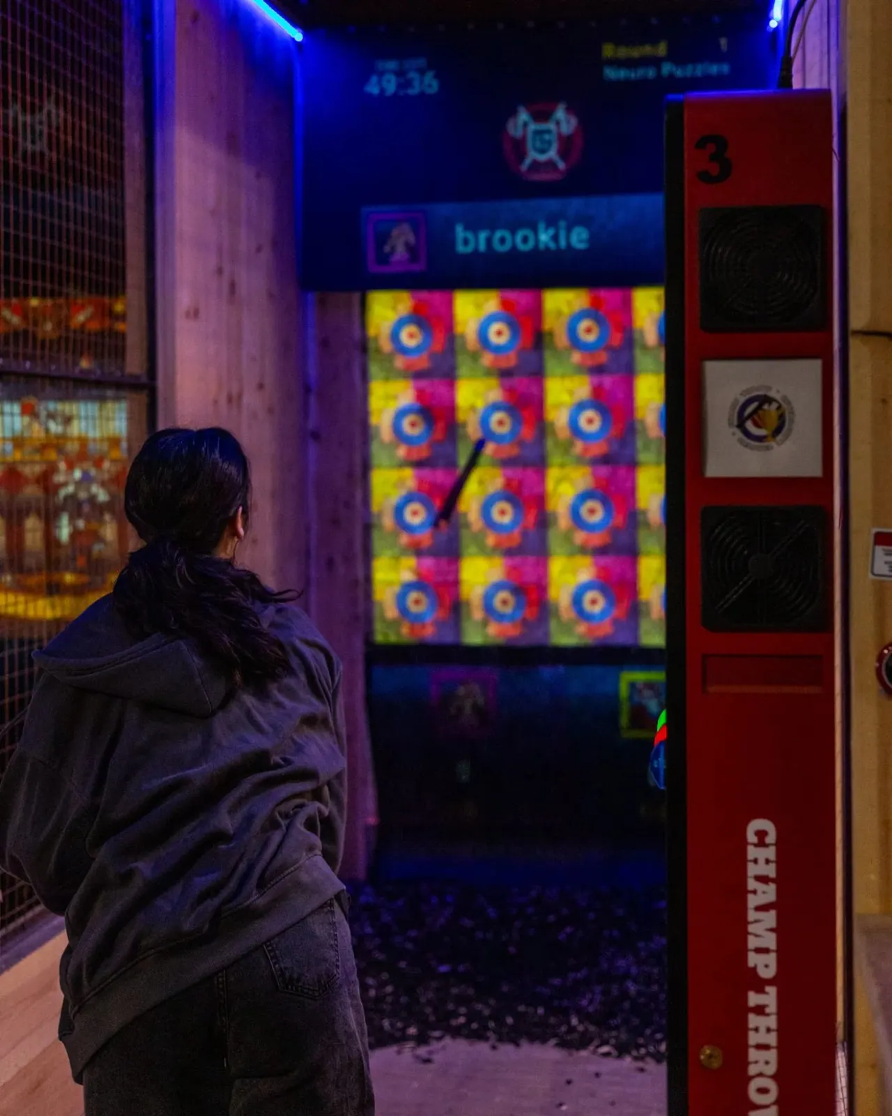 Person playing an arcade game with colourful target display lit by blue and purple neon lighting.