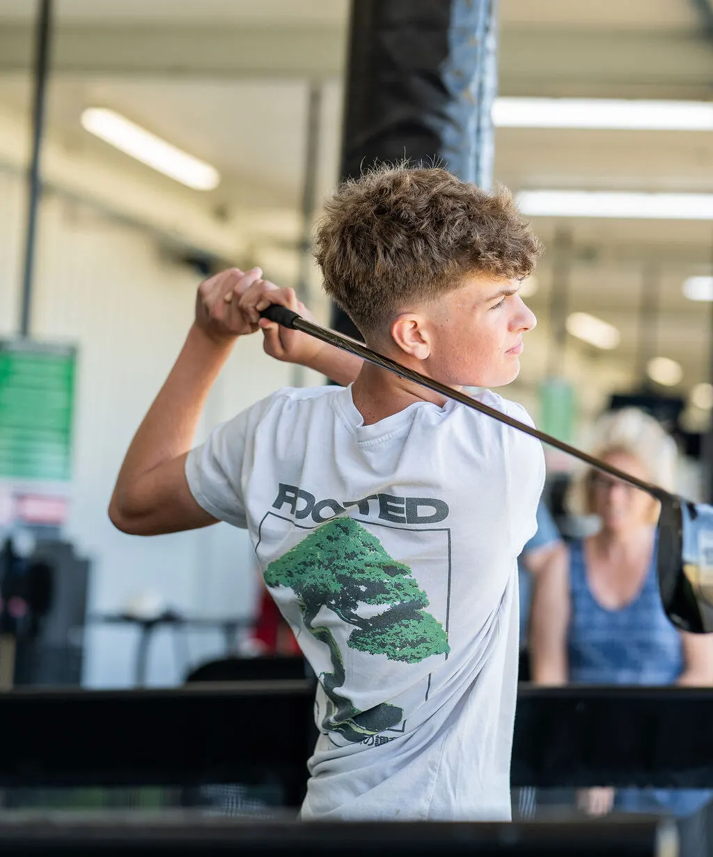 Young person holding a golf club mid-swing indoors at an indoor golf facility.