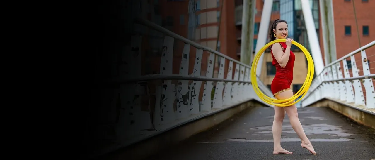 Woman in red costume performing rhythmic gymnastics with a yellow hoop on an urban bridge.