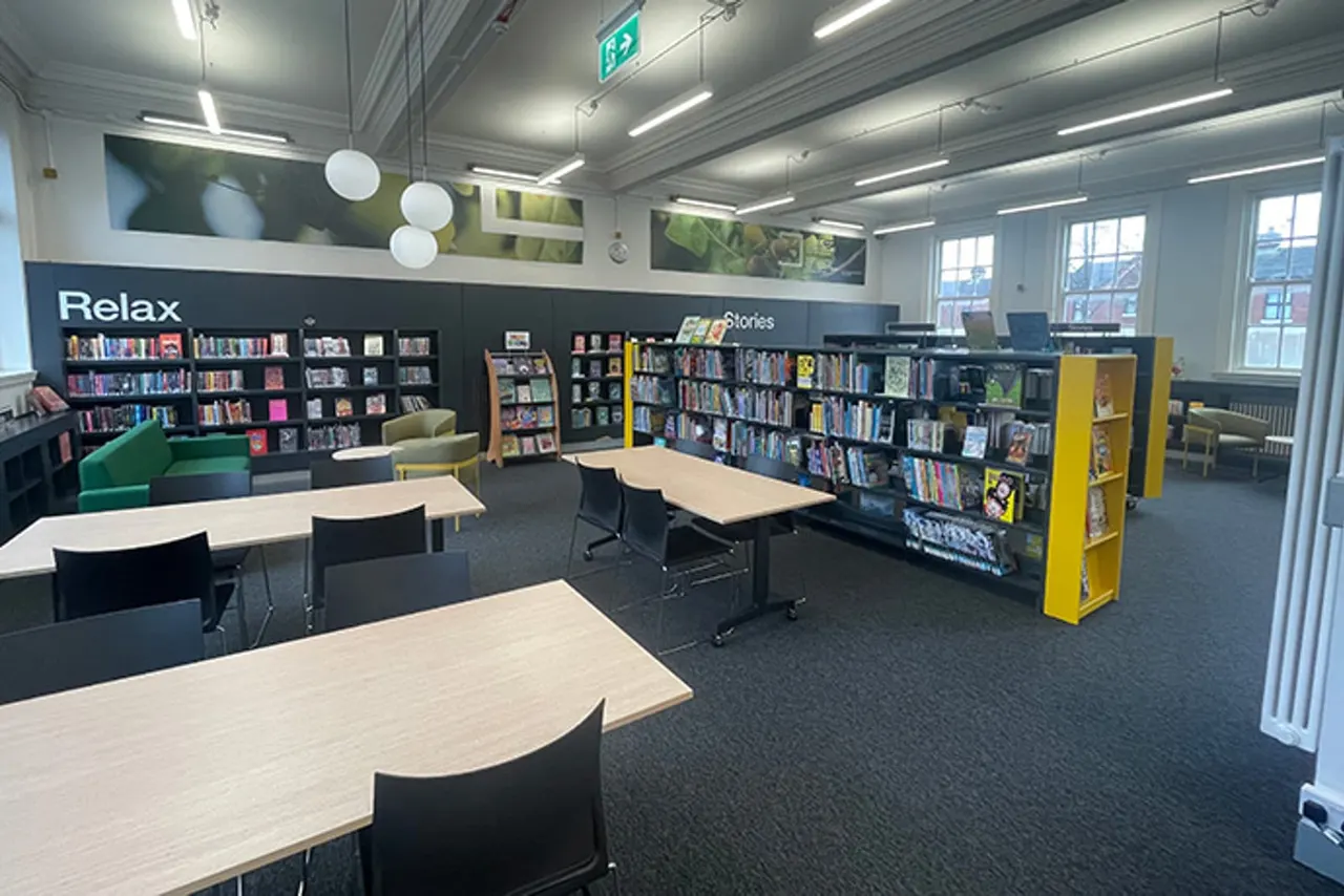 Modern library interior with study tables, bookshelves, and a relaxation area with seating.