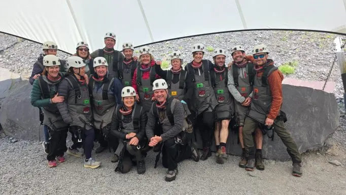 Group of people wearing climbing helmets and safety gear posing together indoors at a climbing wall facility.