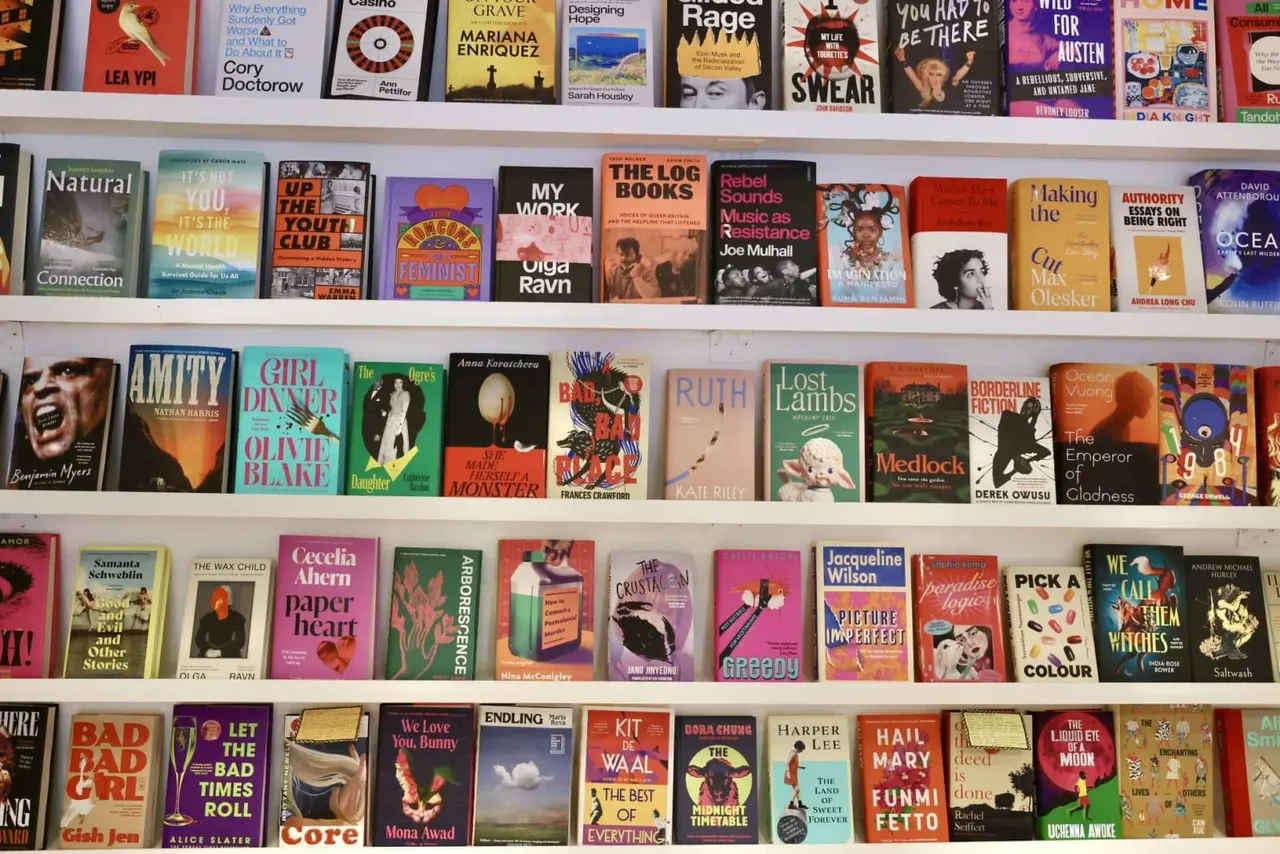Bookshelves displaying a diverse collection of books with colourful spines and covers arranged across four white shelves.
