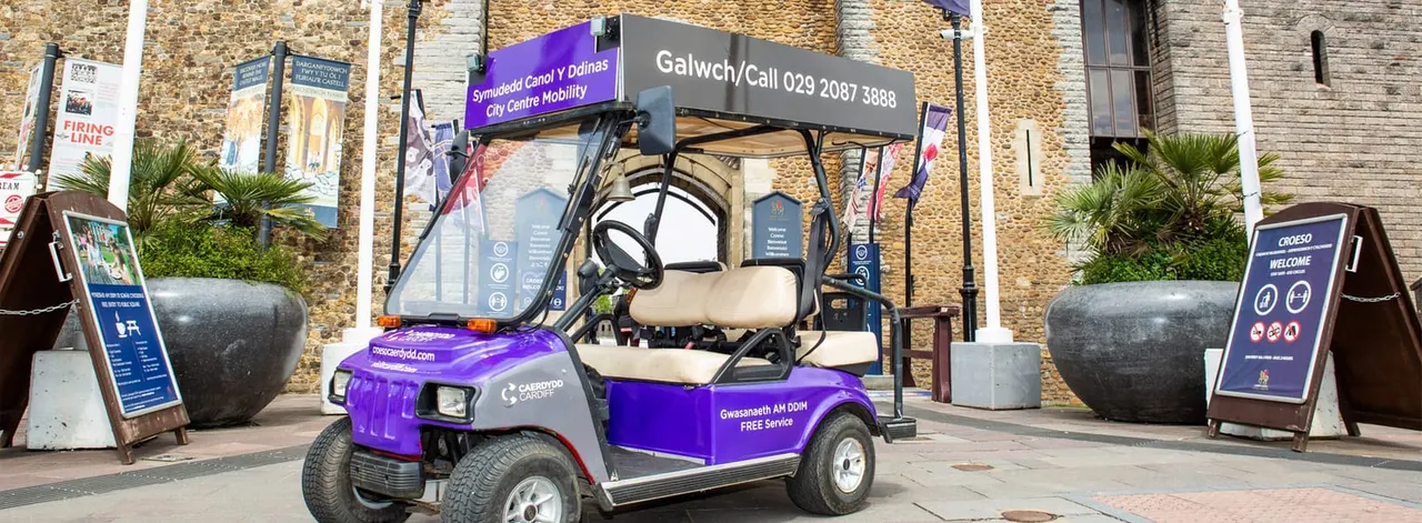 Purple electric mobility vehicle parked outside a historic stone building in a city centre.