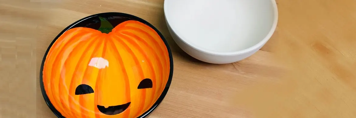 A ceramic plate decorated with a smiling jack-o'-lantern face sits on a wooden table next to an empty white bowl.