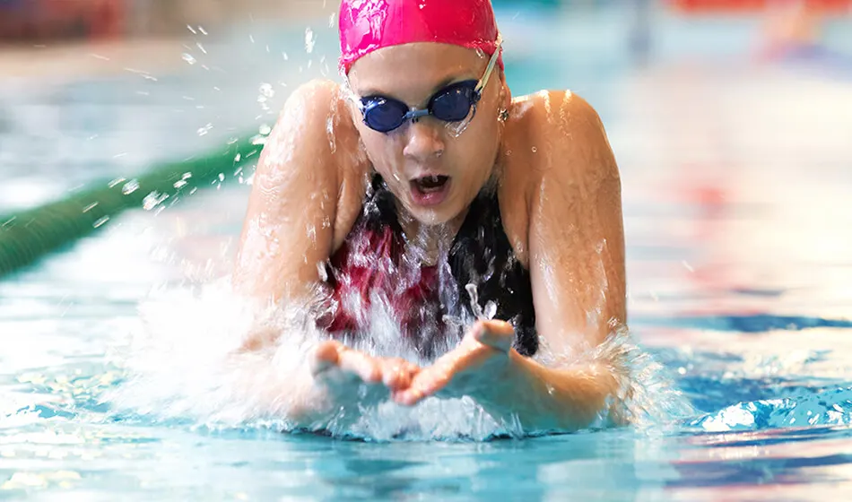 Competitive swimmer performing breaststroke in pool wearing pink cap and goggles.