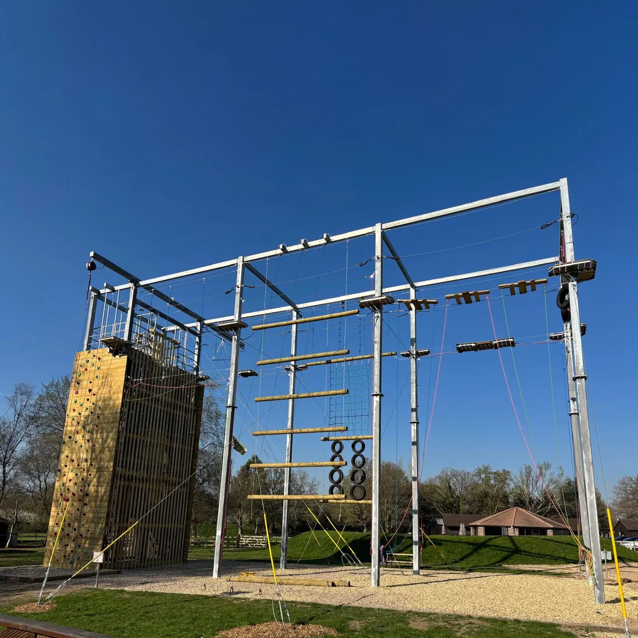 Large outdoor adventure climbing frame with rock wall and multiple rope courses under clear blue sky.