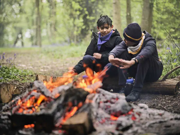 Two people warming their hands by a campfire in a woodland setting.