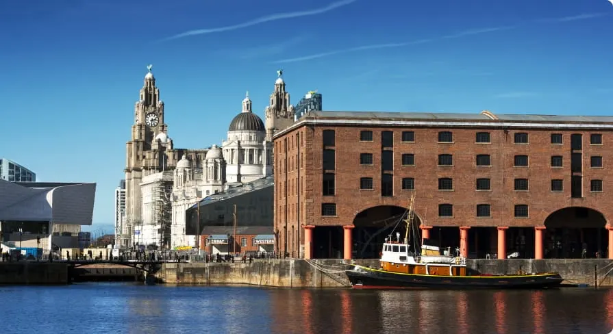A waterfront scene with historic buildings, a cathedral, and a moored vessel on the river under clear blue sky.