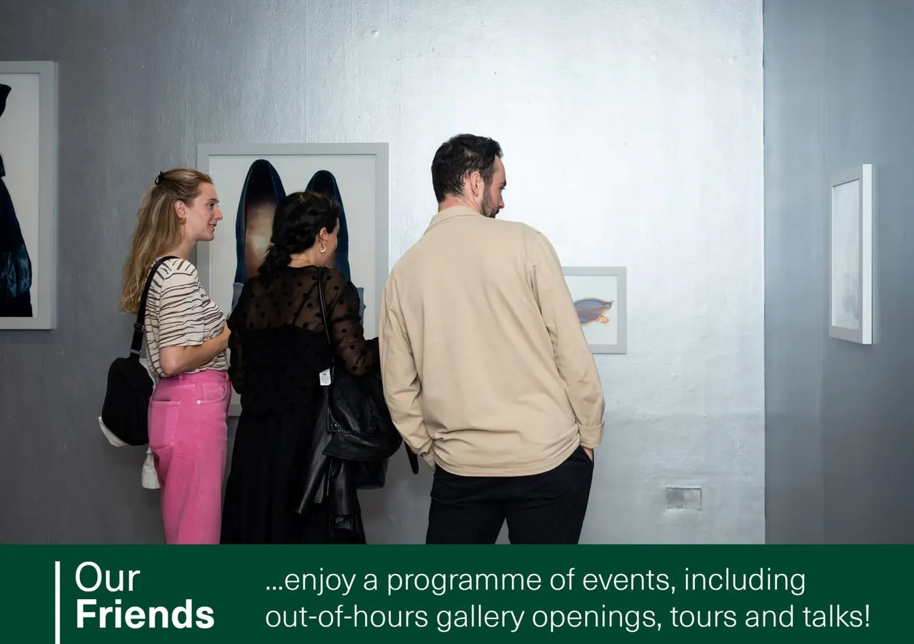Three visitors viewing framed photographs on white gallery walls during an exhibition.