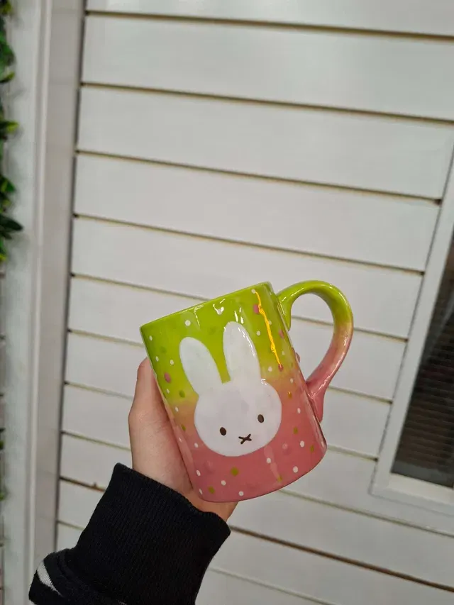Hand holding a decorative ceramic mug with a bunny design and gradient green-to-pink glaze.