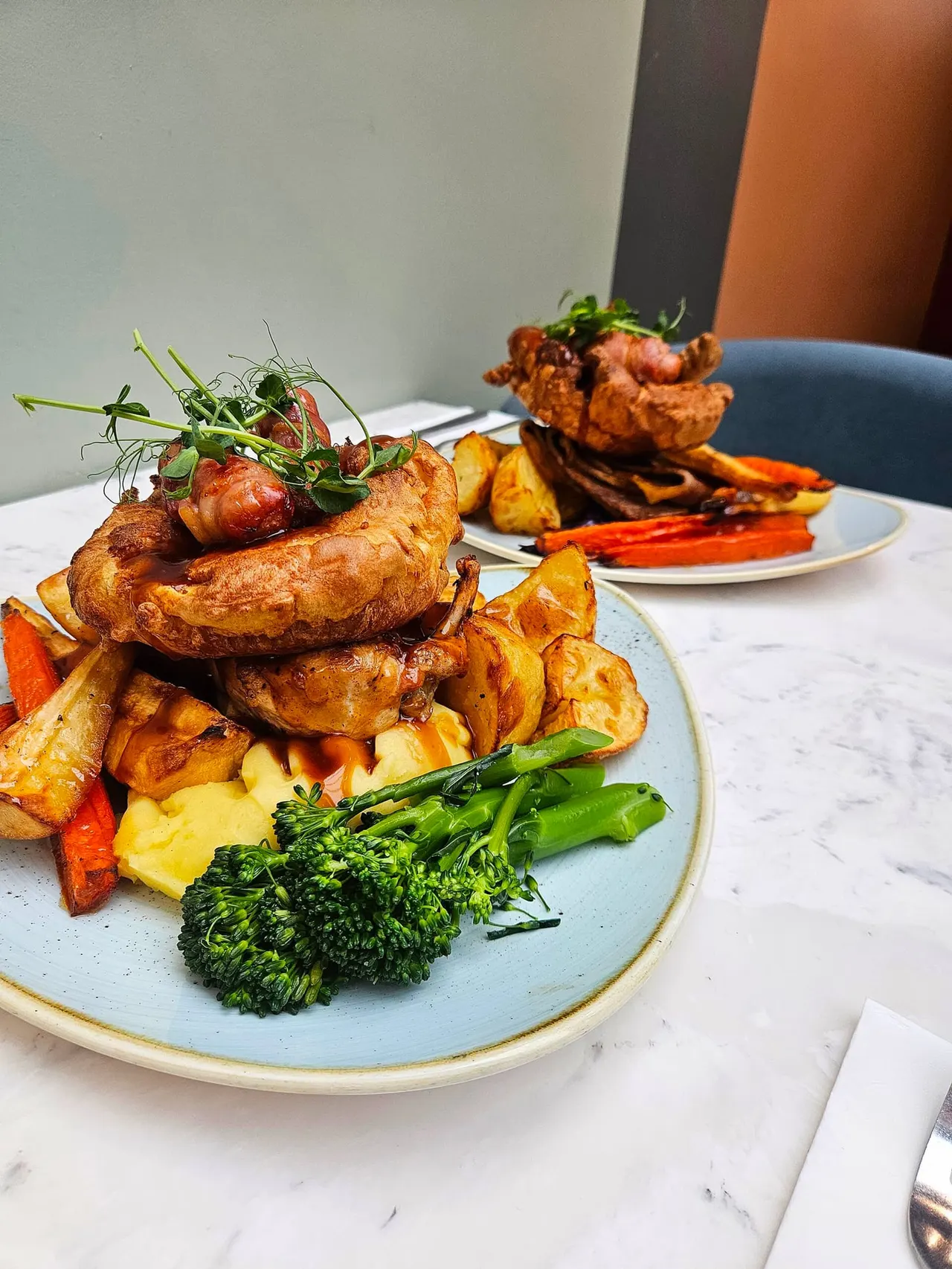 Two plates of roasted sausages with crispy potatoes, roasted vegetables and broccoli garnished with microgreens.