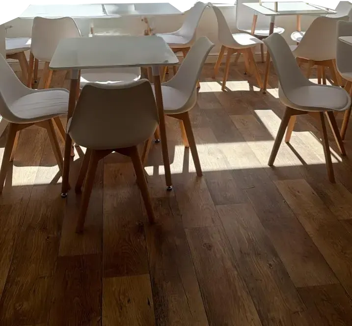 Bright dining area with modern white chairs and wooden-legged tables on wooden flooring, sunlit through skylights.