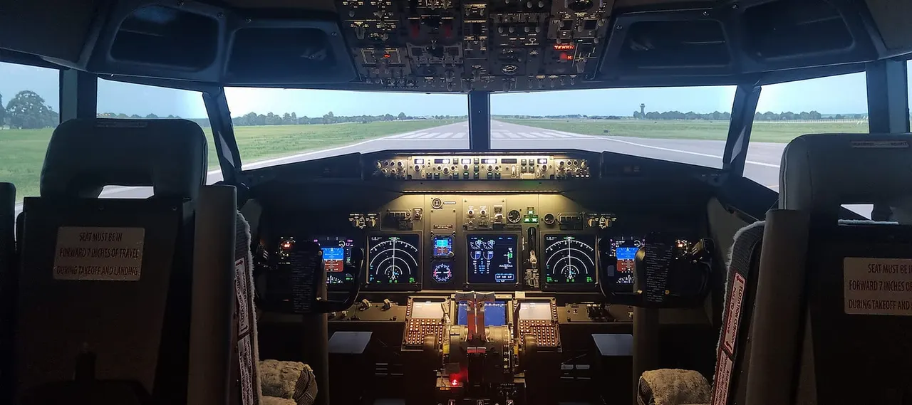 Interior of aircraft flight simulator cockpit with runway visible through windscreen ahead.