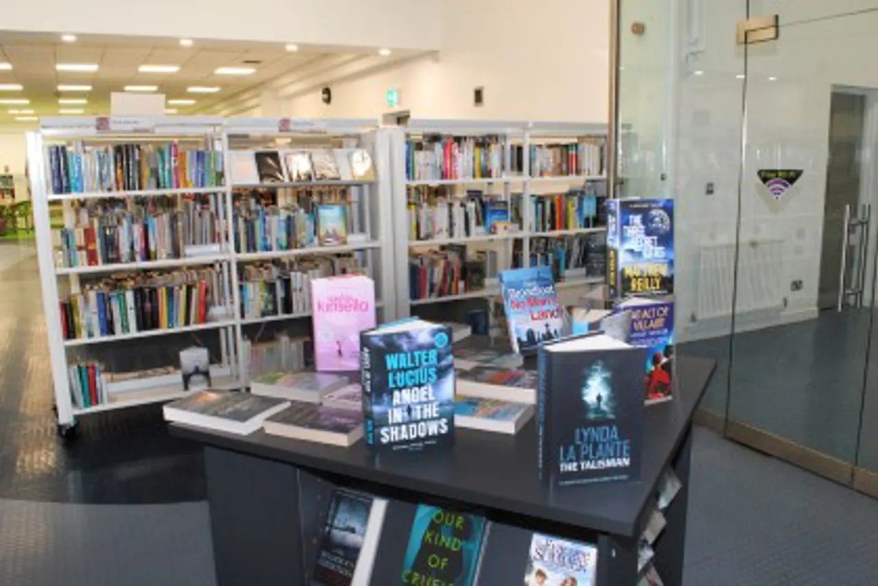 Modern library interior with white shelving units displaying books and a central black display table featuring featured titles.