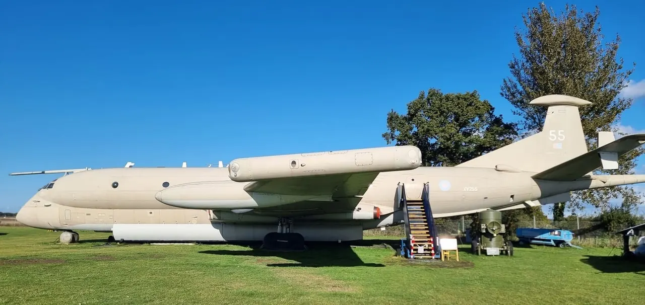 A large decommissioned military transport aircraft displayed on grass with an entrance stairway beneath clear blue sky.