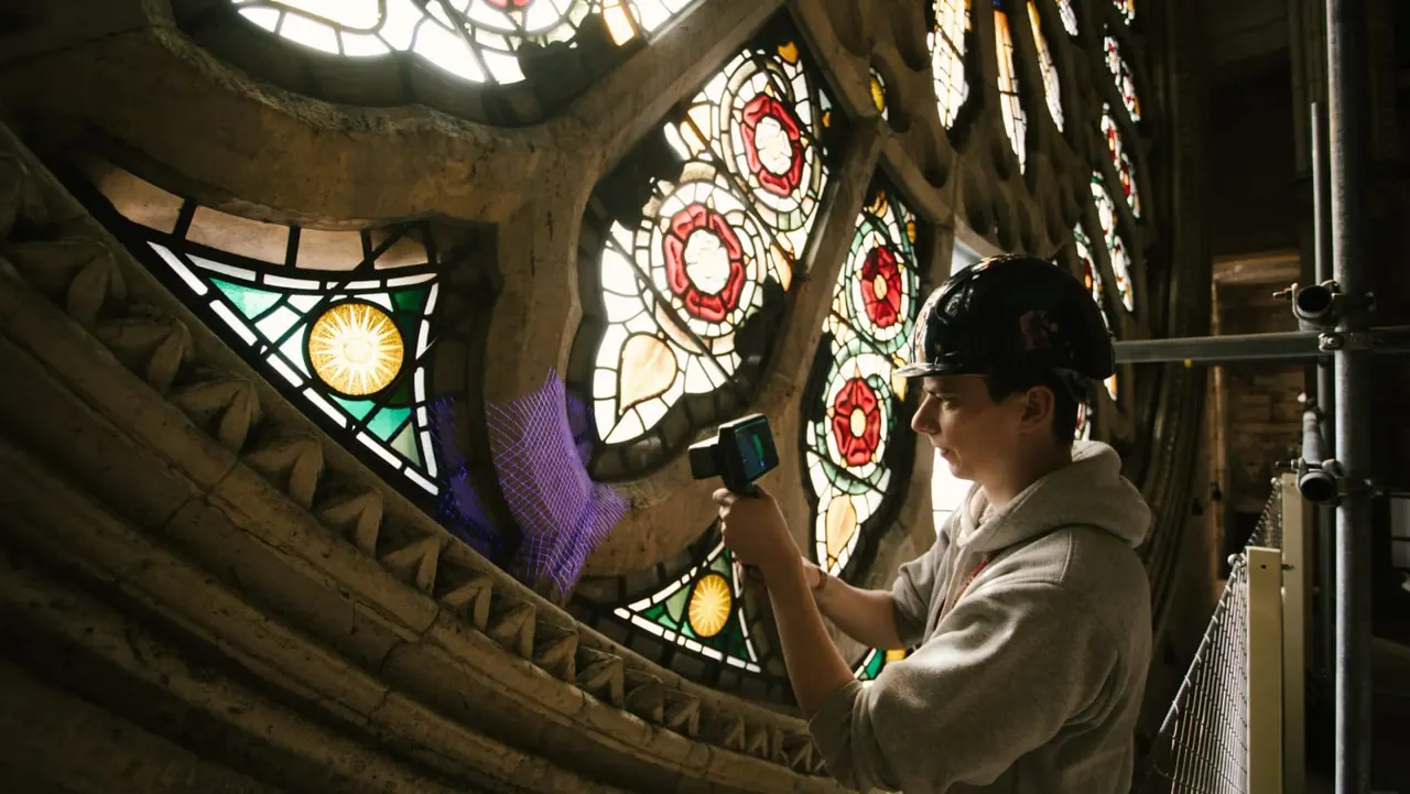 Person photographing ornate stained glass windows with red and yellow patterns inside a historic stone building.