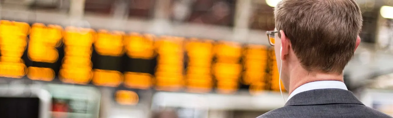 Man in business attire viewing an illuminated yellow digital display board.