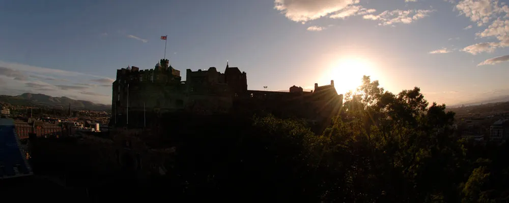 Medieval castle silhouetted against sunset sky with city sprawling below.