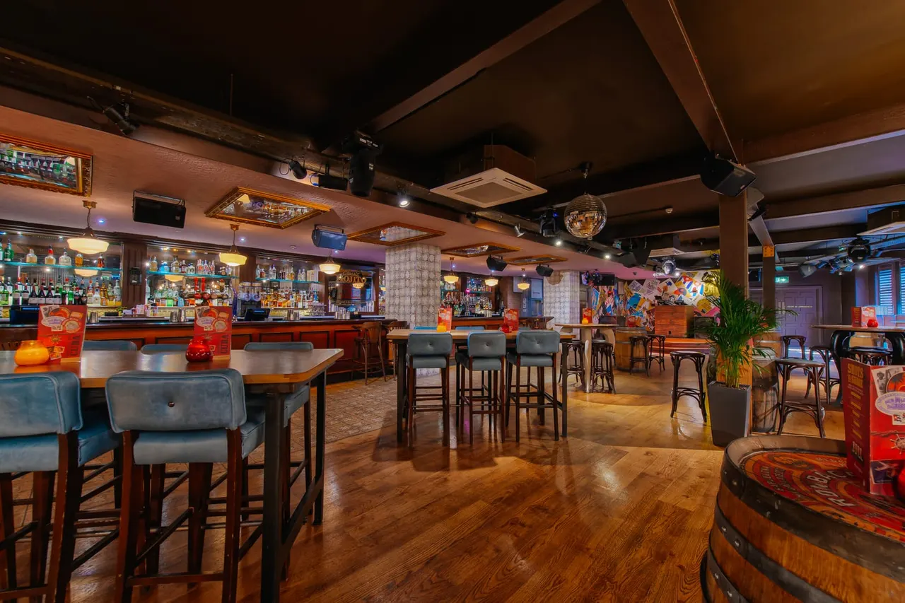 Interior of a vibrant bar and restaurant with wooden floors, high seating at bar counters, and colourful Cuban-themed décor throughout.