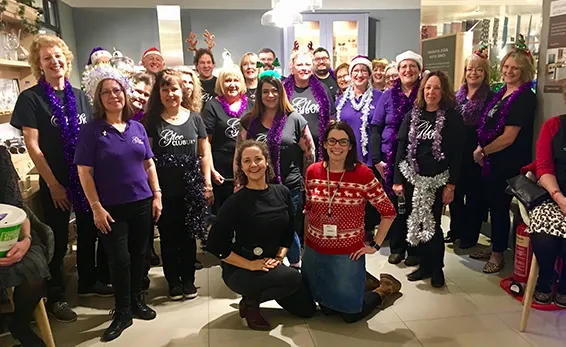 Large group of adults wearing purple and black clothing gathered indoors for a choir photo.