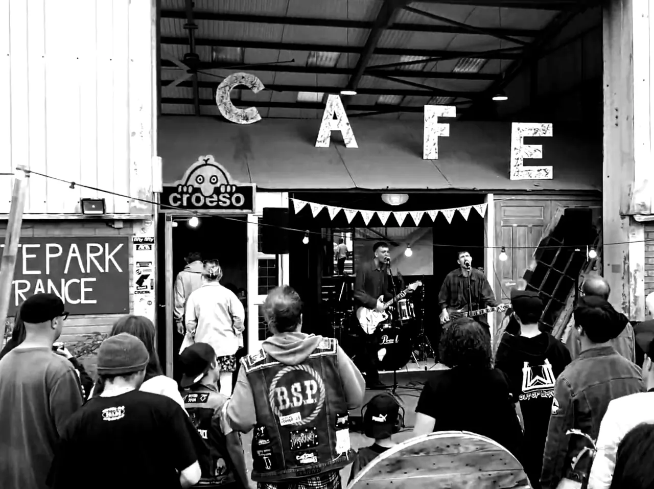 Live band performing on stage at an indoor venue with crowd gathered in front watching musicians play guitars and drums.