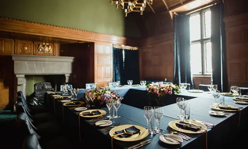 Formal dining room with long table set for an event, fireplace, and ornate wooden panelling.