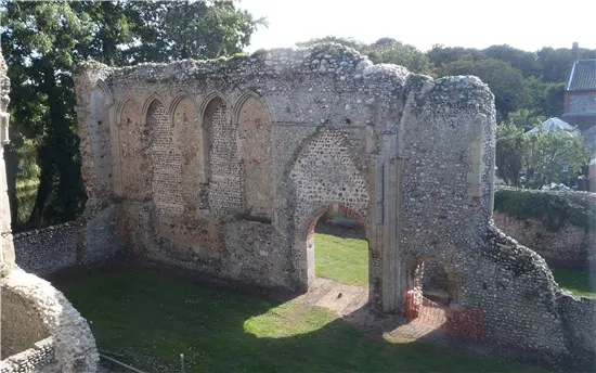 Ruins of a medieval stone gatehouse with arched entrance and windows, surrounded by grassy grounds and trees.