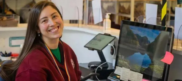 Young woman smiling at camera with geological display screens and museum exhibits in background.