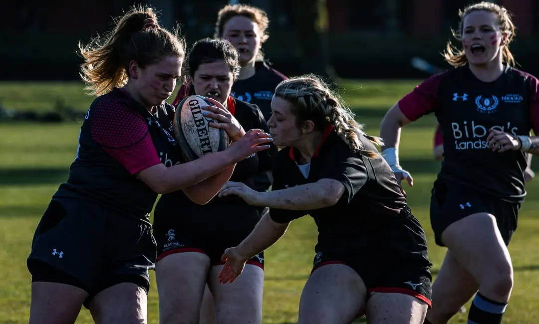 Young female rugby players competing for the ball during a match on a grass field.
