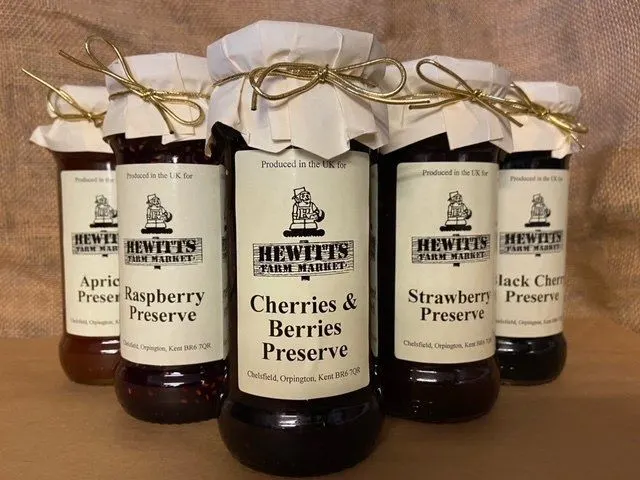 Five jars of Hewitt's Farm Market preserves with white fabric tops and gold twine bows, arranged on a textured background.