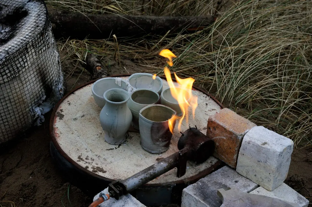 Ceramic vessels heating over an open fire in a primitive kiln setup outdoors.